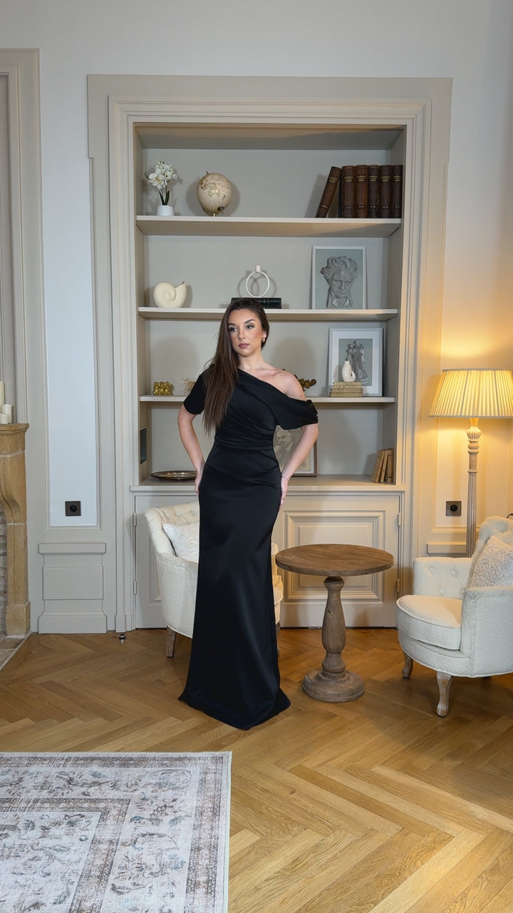 Robe de soirée noire chic au col asymétrique, sans manches et sans fente. Une robe élégante et moderne pour vos soirées raffinées.